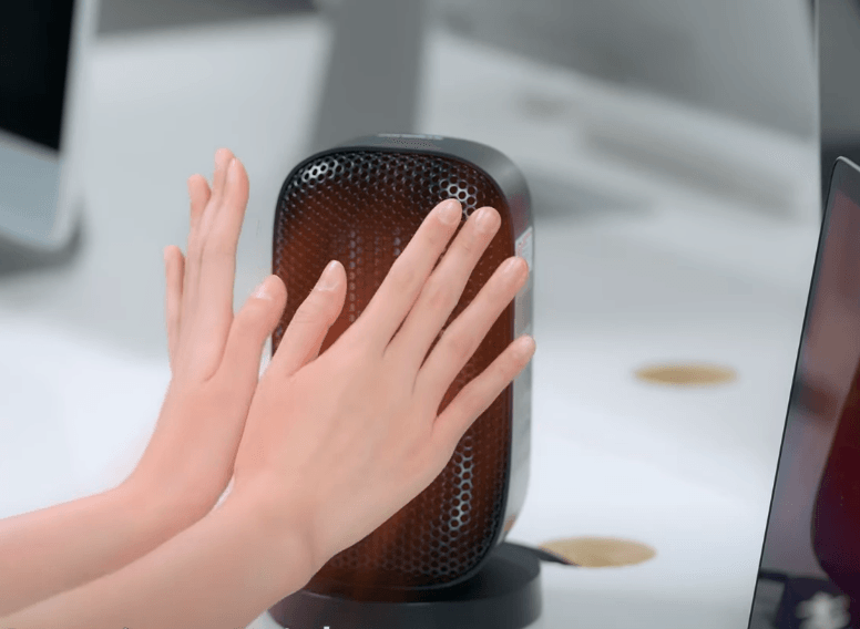A pair of hands being warmed up by a Senelux desk top space heater in a home office setting