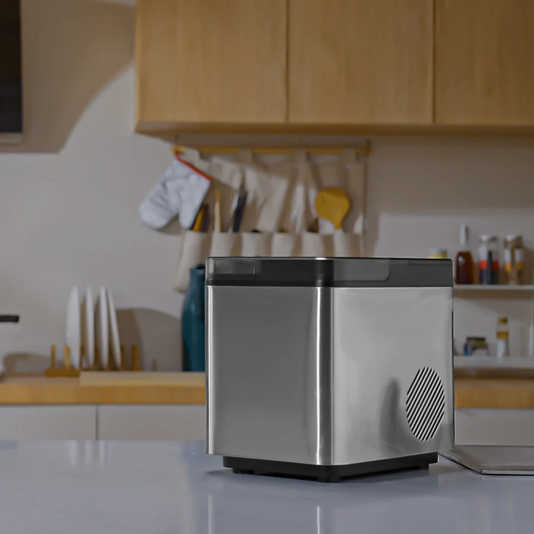 A hand using a clean white scoop to collect ice from a Senelux Compact Ice Maker.